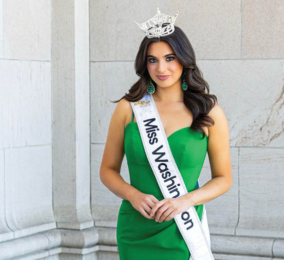 Una mujer está de pie con los brazos cruzados junto a una ventana.